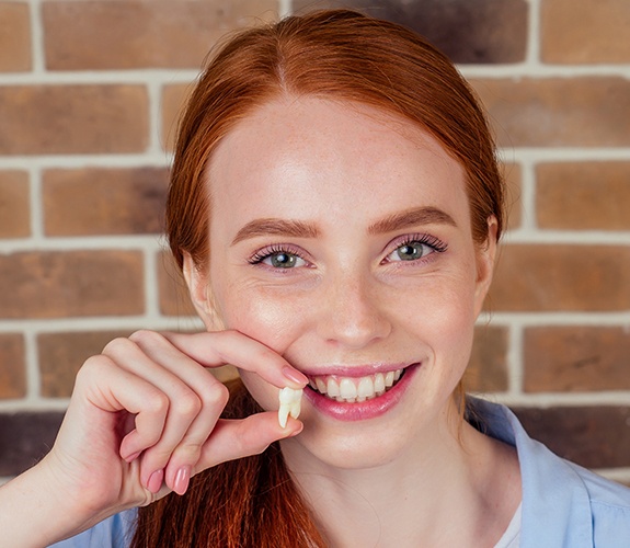 Woman smiling after tooth extraction and holding her tooth