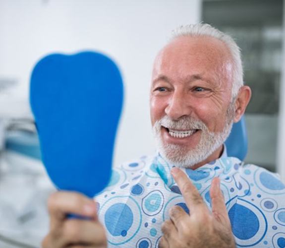 man with dental implants  in Wilmington smiling in front of a mirror