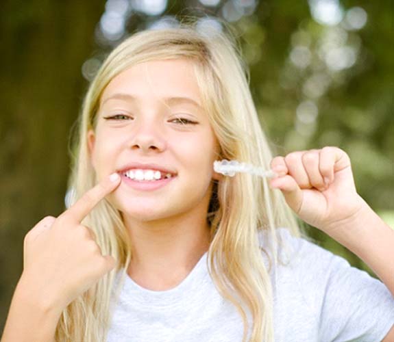 Young girl with Invisalign Teen in Wilmington pointing to her smile