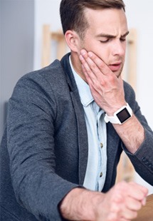 Man holding his jaw while working at his desk
