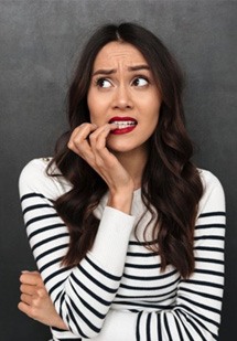 Woman biting her nails on gray background