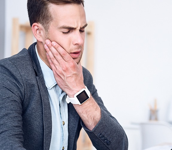 Man in need of T M J treatment holding his jaw