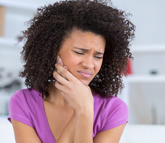 Woman in need of root canal therapy holding cheek in pain