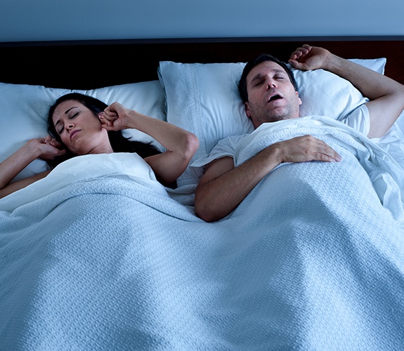 Frustrated woman in bed next to snoring man